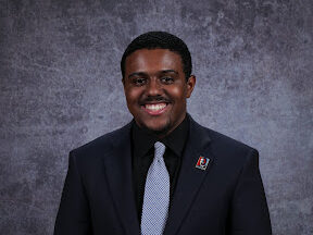 Nate Woodard, a man in a tie and jacket against a grey background.